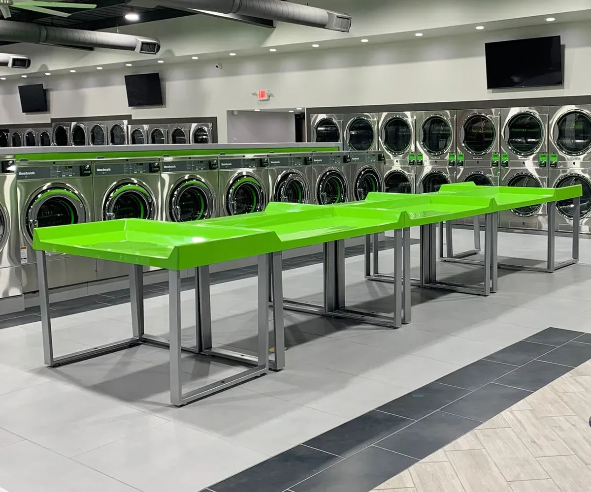 Spacious laundry floor with green folding tables, laundry carts, and rows of modern machines.