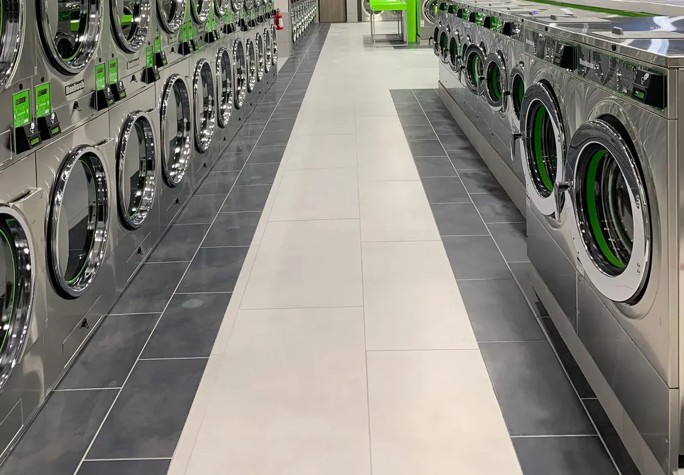 Long, clean aisle between rows of stainless-steel laundry machines.