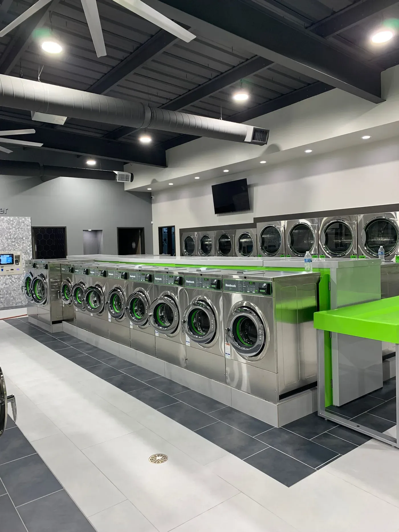 Bright, clean Space City Laundry interior with rows of stainless-steel washers and dryers.