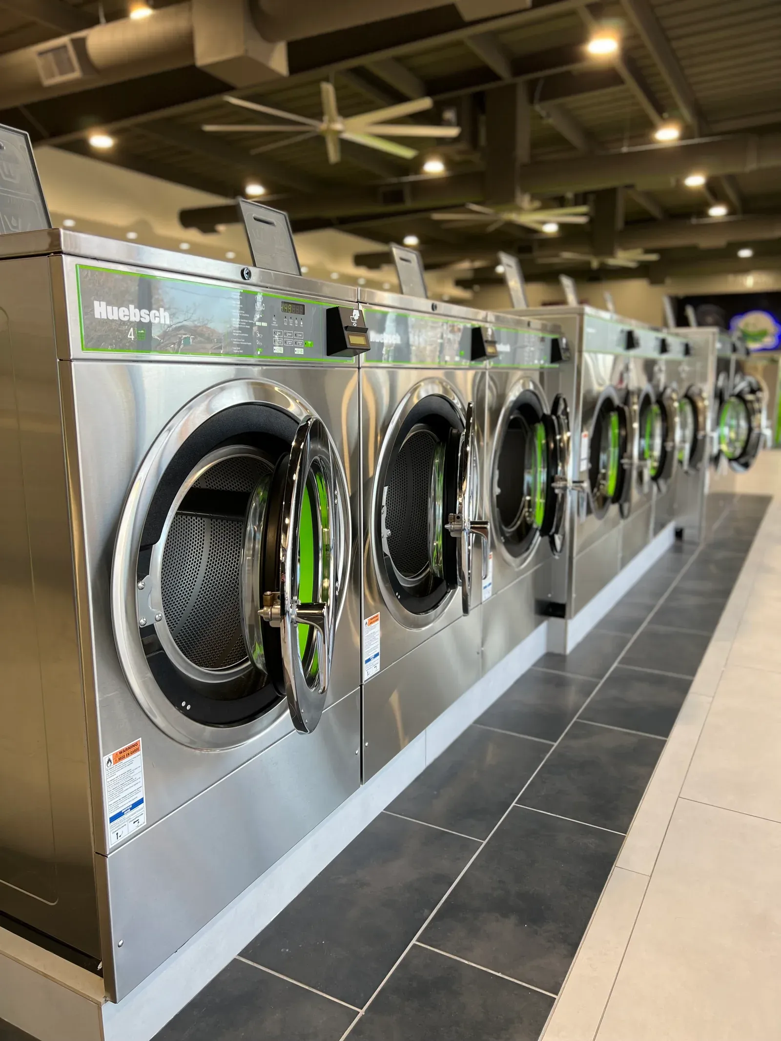 Close-up row of stainless-steel washers and dryers inside Space City Laundry.